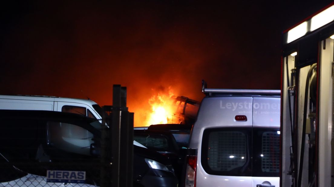 Met een heftruck worden auto's weggehaald van het terrein van de autosloperij in Oosterland waar een grote brand woedt.