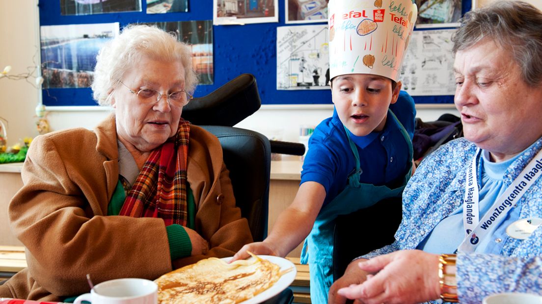 Kinderen bakken pannekoeken voor ouderen.