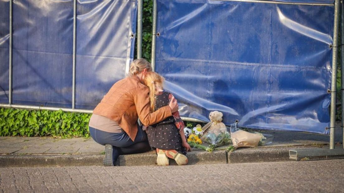 Een vrouw en kind leggen bloemen en een knuffel bij de afzetting in Geldermalsen.