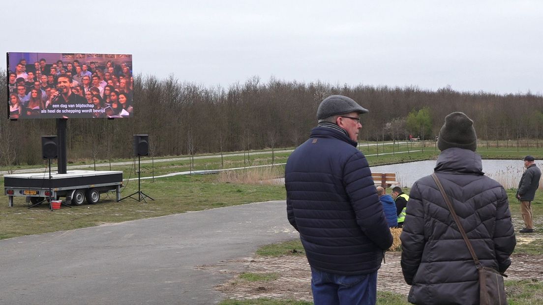 Bezoekers volgen de openluchtdienst op een groot scherm