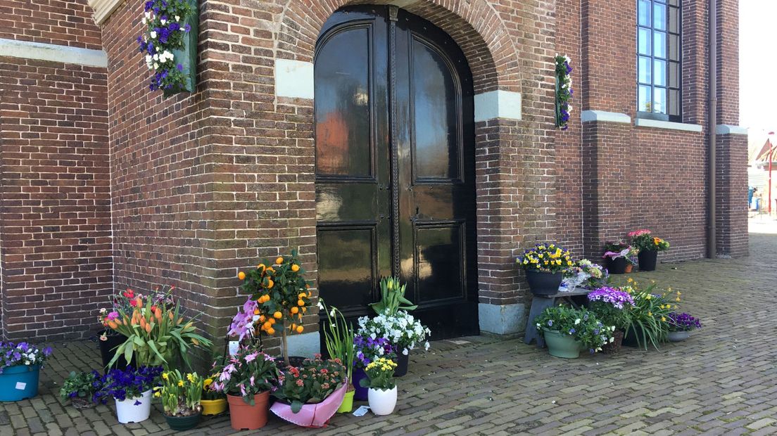 Voor de deur van de kerk staan bloemen, achtergelaten door mensen uit de gemeenschap.