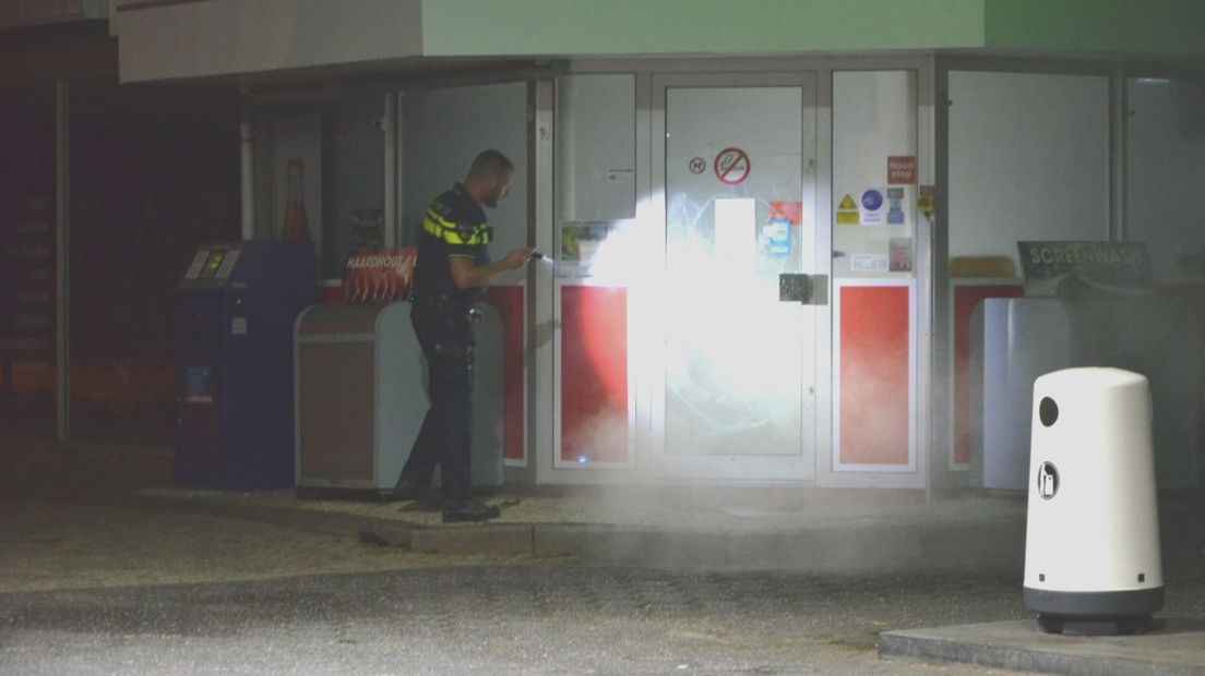 Een agent schijnt met zijn zaklamp op een ingeslagen ruit, waar de rook uit komt