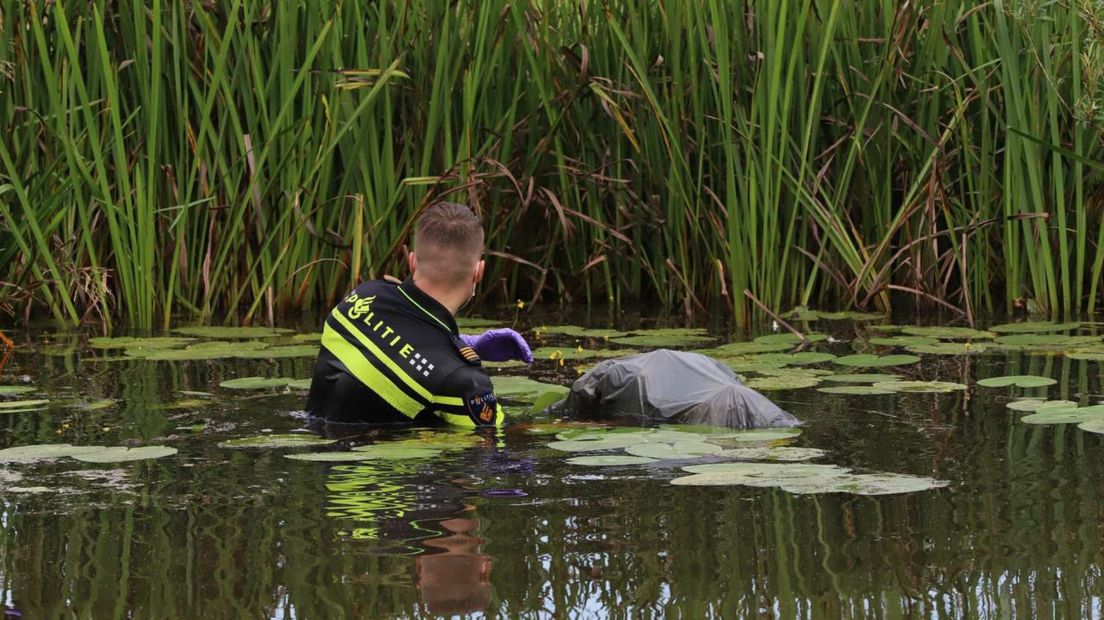 Een agent staat diep in het Kieldiep om een vuilniszak te pakken