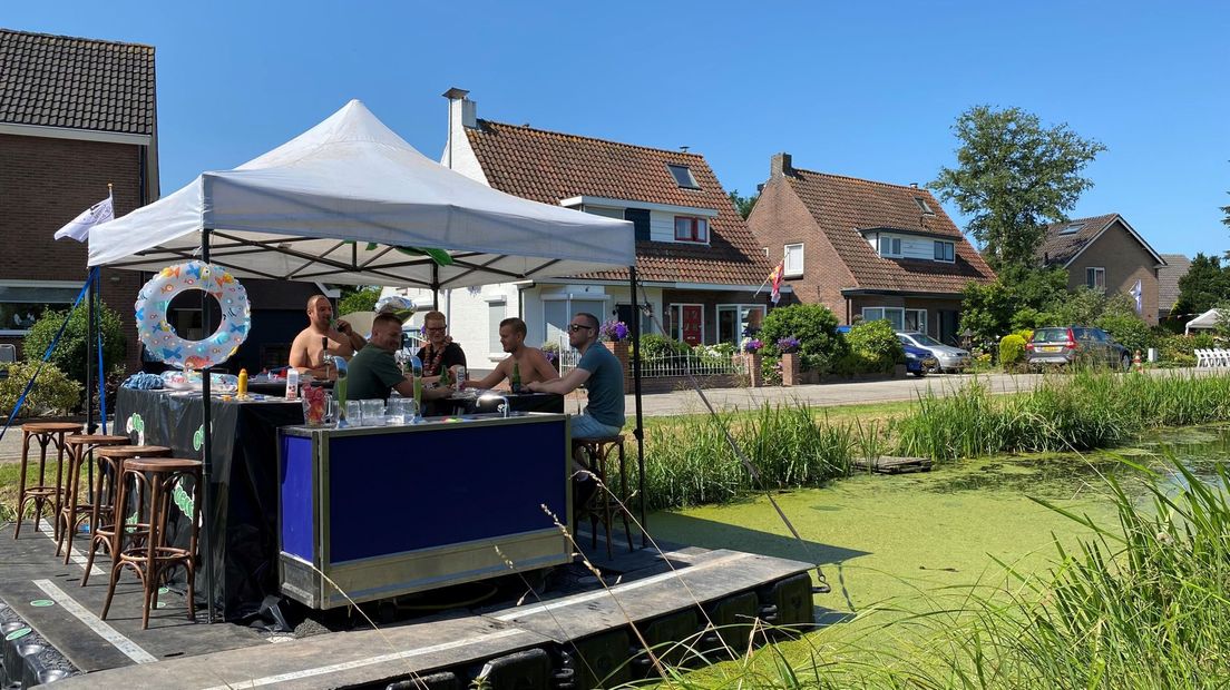 Deze mannen wachten op een drijvend terras op de renners die meedoen aan het wielerevenement Tour de Schalkwijk. Het is even voor de middag.