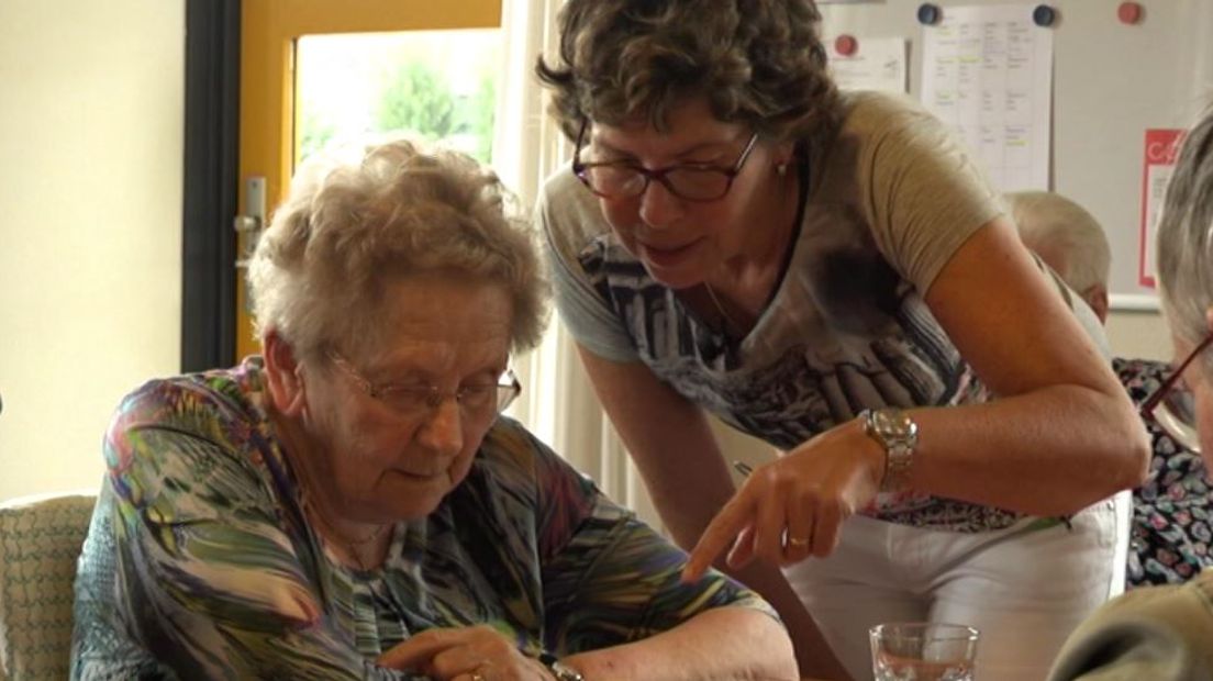 Een groepje dames speelt vanmorgen in Mariënvelde Rummikub. Activiteitenbegeleidster Anita Reukers helpt de dames een handje. In een hoekje zit mevrouw Klein Goldewijk een geel/groene das te breien. 'Ik brei elke dag', zegt ze. 'En ik vind het gezellig om dat hier te doen met allemaal mensen om me heen, ik ben namelijk alleen, snap je?'