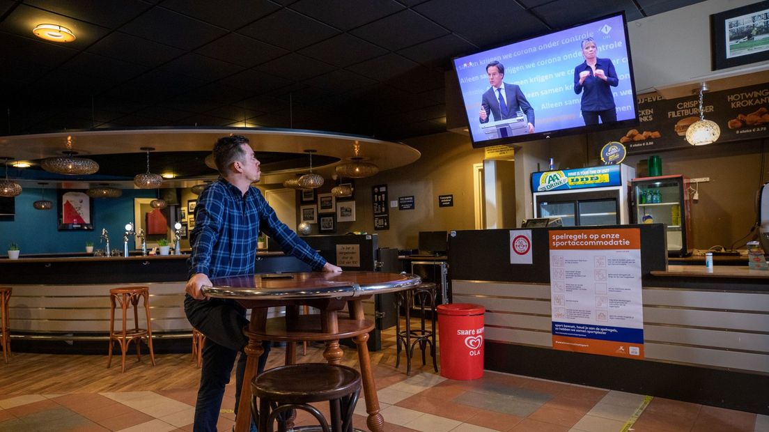 Deze voorzitter van een voetbalclub bekijkt de persconferentie vanuit de sportkantine