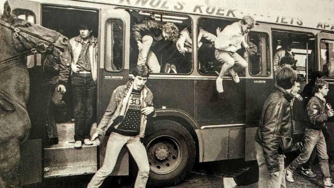 Voetbalsupporters stappen de bus uit, deels leesbaar de slogan van Knol