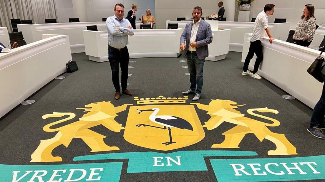 Raadsleden Richard de Mos en Rachid Guernaoui bij het stadswapen van Den Haag in de raadzaal