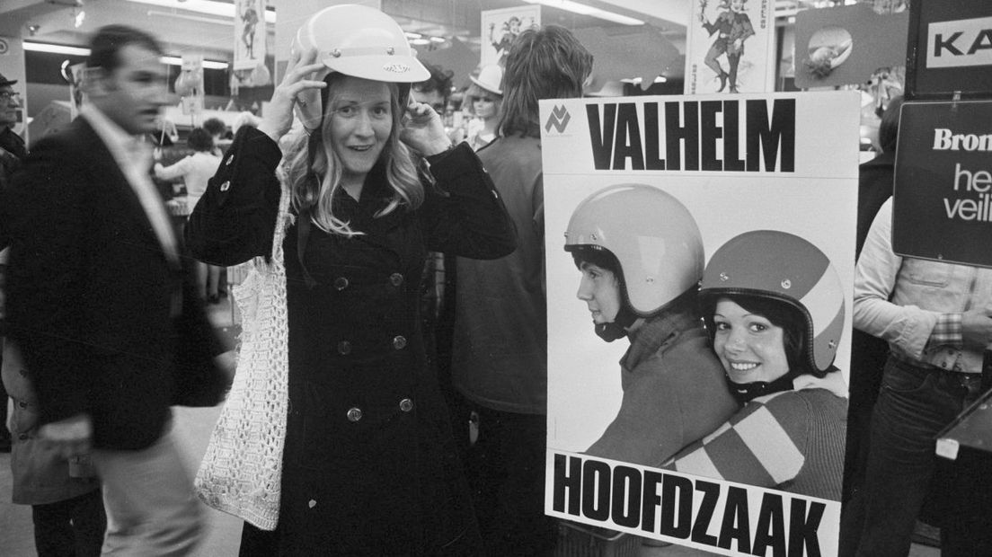 Een vrouw past een helm in de winkel op de eerste dag na de invoering van de helmplicht op brommers in 1975