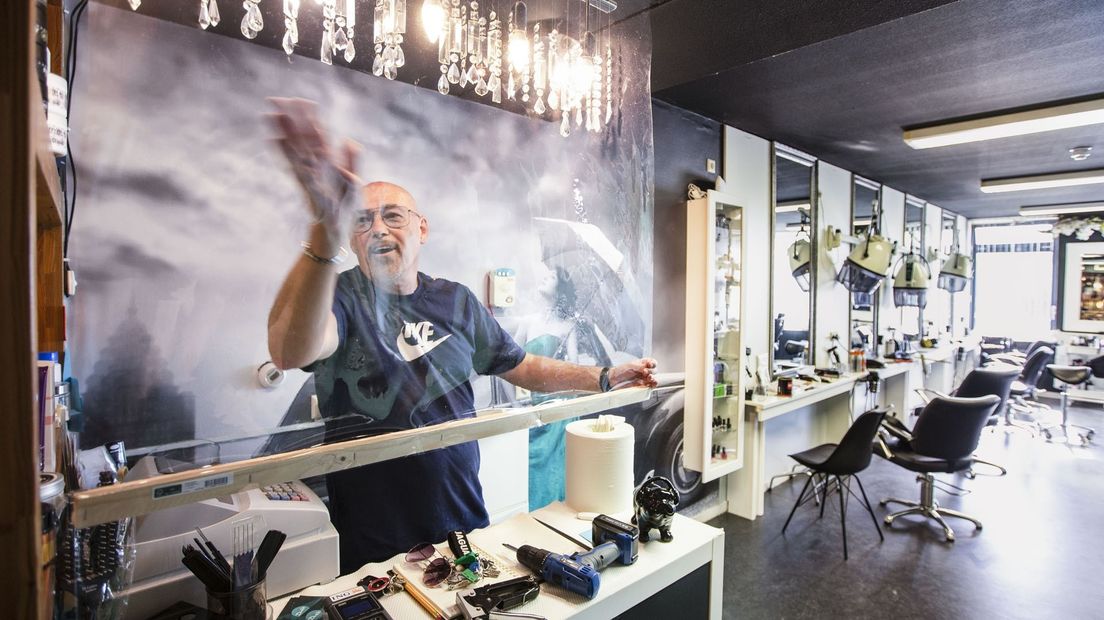 Een kapper hangt plastic schermen op in zijn zaak