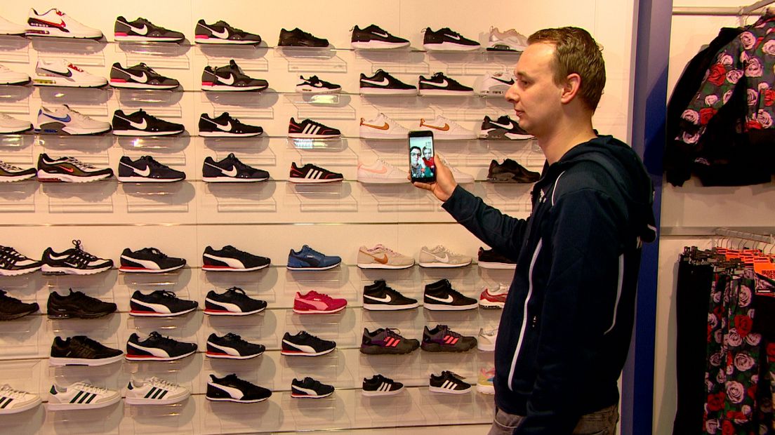 Medewerker Rob van der Sleen laat de schoenencollectie aan de klant zien via zijn telefoon