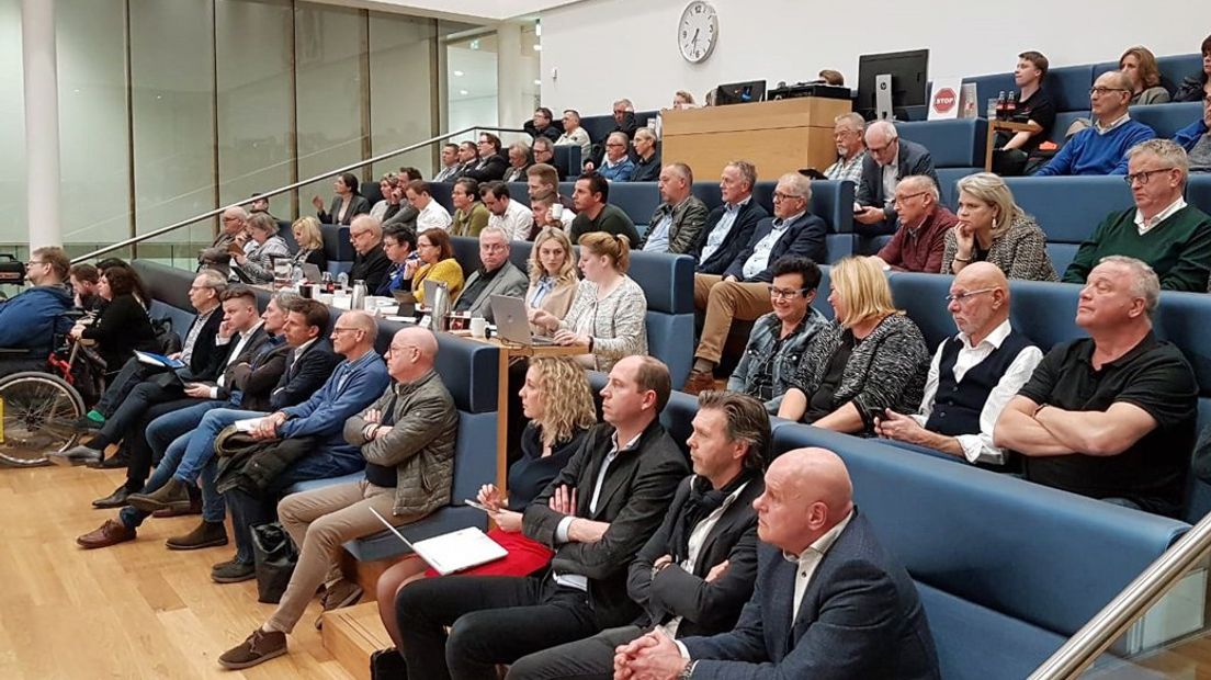 Veel demonstrerende Maasdijkers volgen de vergadering op een scherm