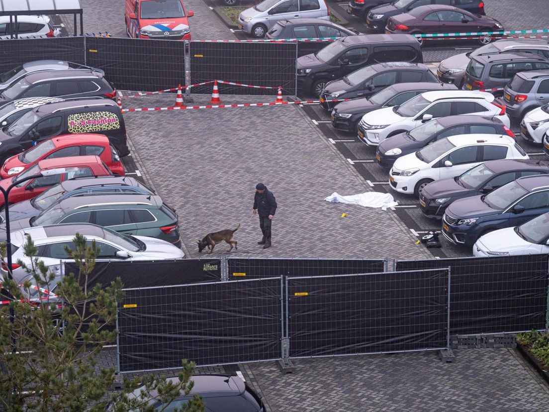 De politie is met een speurhond op zoek naar hulzen op de parkeerplaats