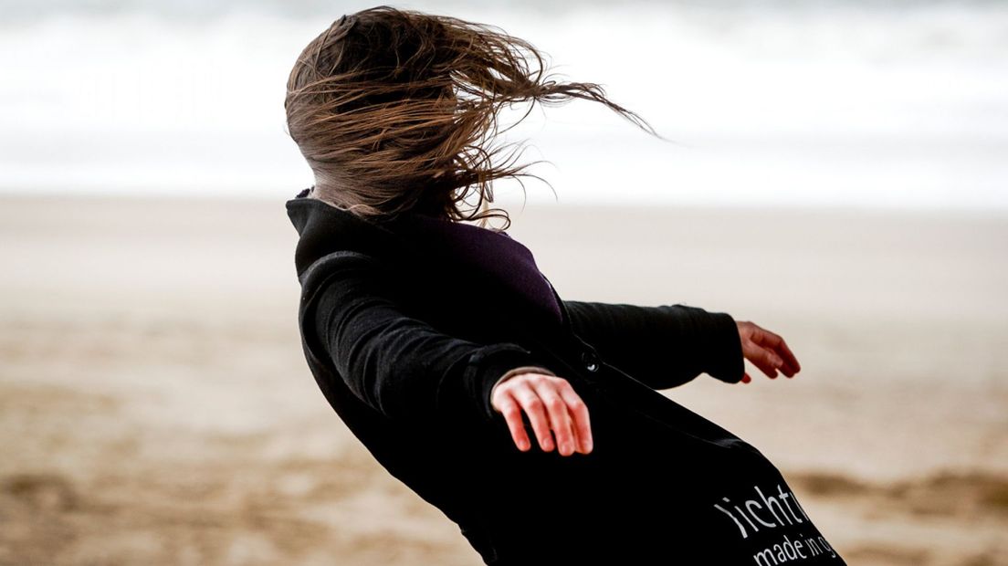 Een vrouw geniet van de harde wind op het strand van Scheveningen