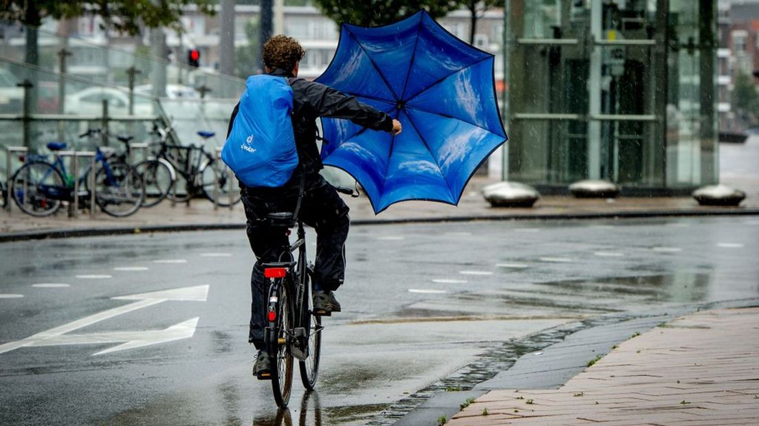 Een fietser probeert zich met een paraplu te beschermen tegen de regen