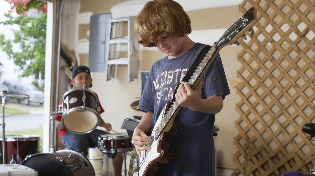 Happy young boy playing guitar with friend drumming in background