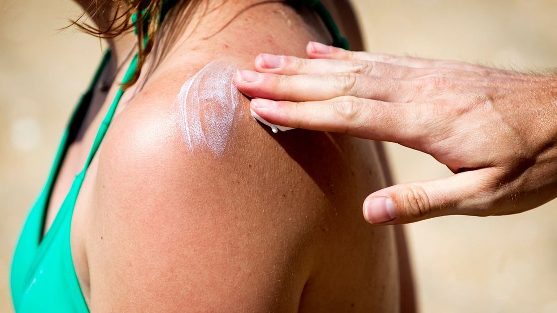 Een vrouw wordt op het strand ingesmeerd.