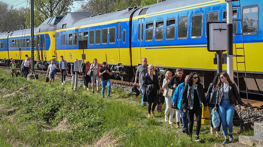 Reizigers gaan te voet verder naast de stilstaande trein in Alphen aan den Rijn.