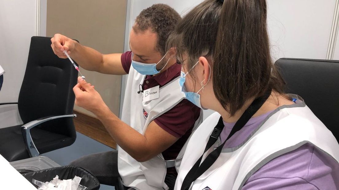 Verpleegkundige Brandon Becker leert zijn collega hoe je extra vaccin uit een flesje kan halen.