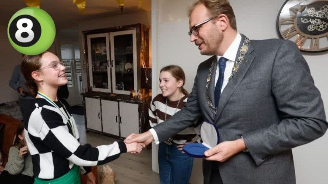 Evi krijgt van burgemeester Mark Boumans een jeugdlintje voor haar bierdopjesactie voor KiKa.