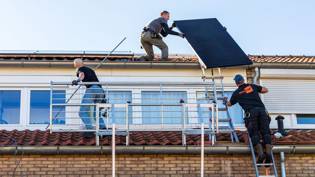 Medewerkers van een installatiebedrijf leggen zonnepanelen op het dak van een woning.