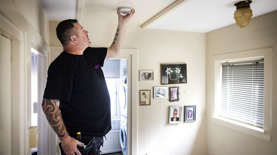 Een installateur plaatst een rookmelder in een woning